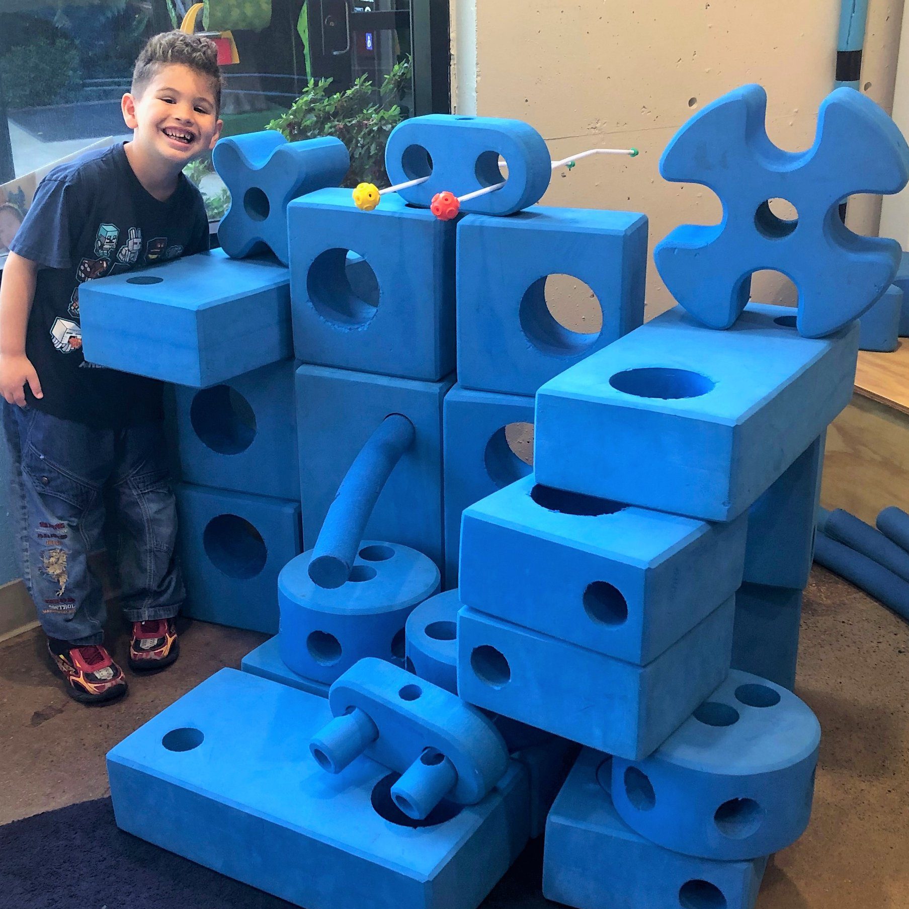 A boy smiles next to a fort made of blue blocks