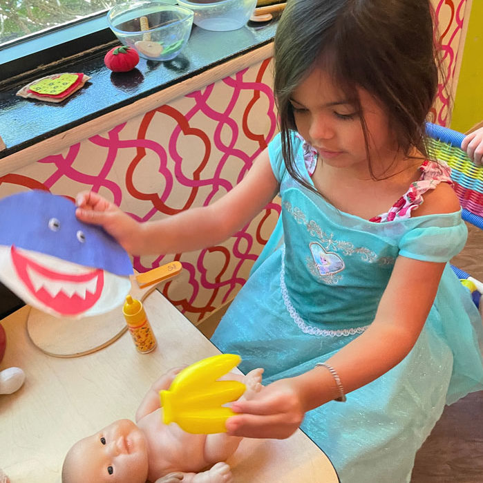 A girl plays with a baby doll and paper shark in our playhouse area.