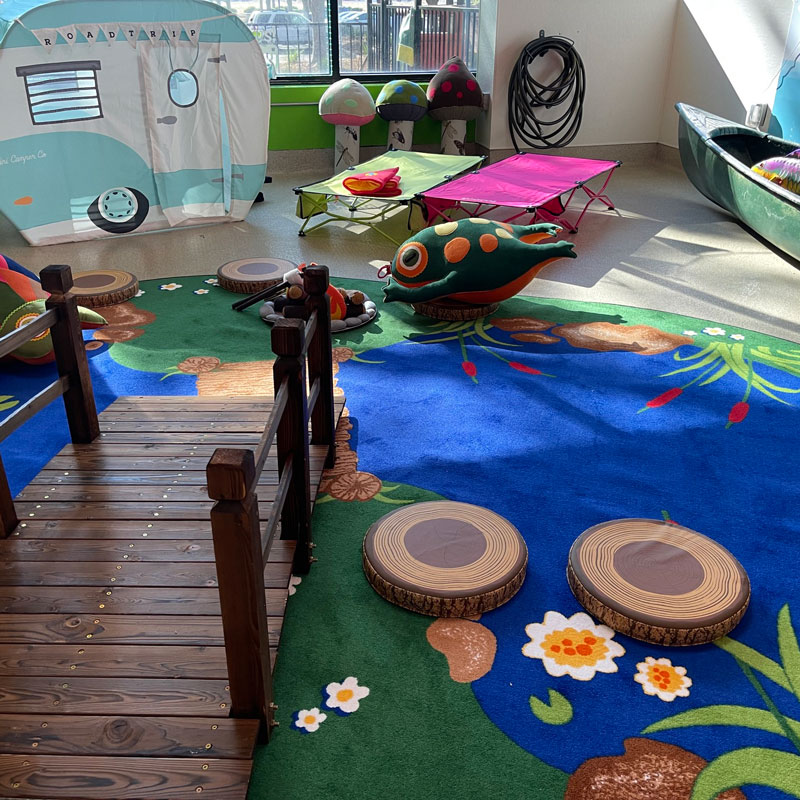 A mock campsite area is shown with a bridge, play rv, frog stuffed animals and cots.