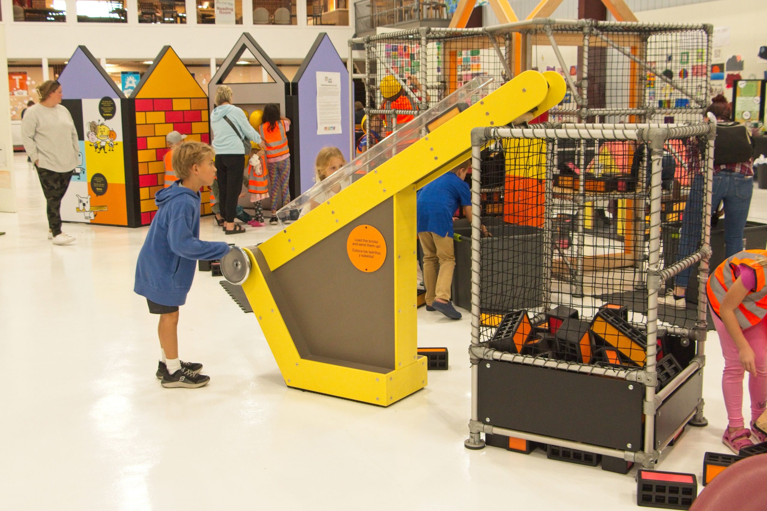 A boy in a blue sweatshirt turns the handle of a ramp moving a block upwards, leading to a big holder of building blocks