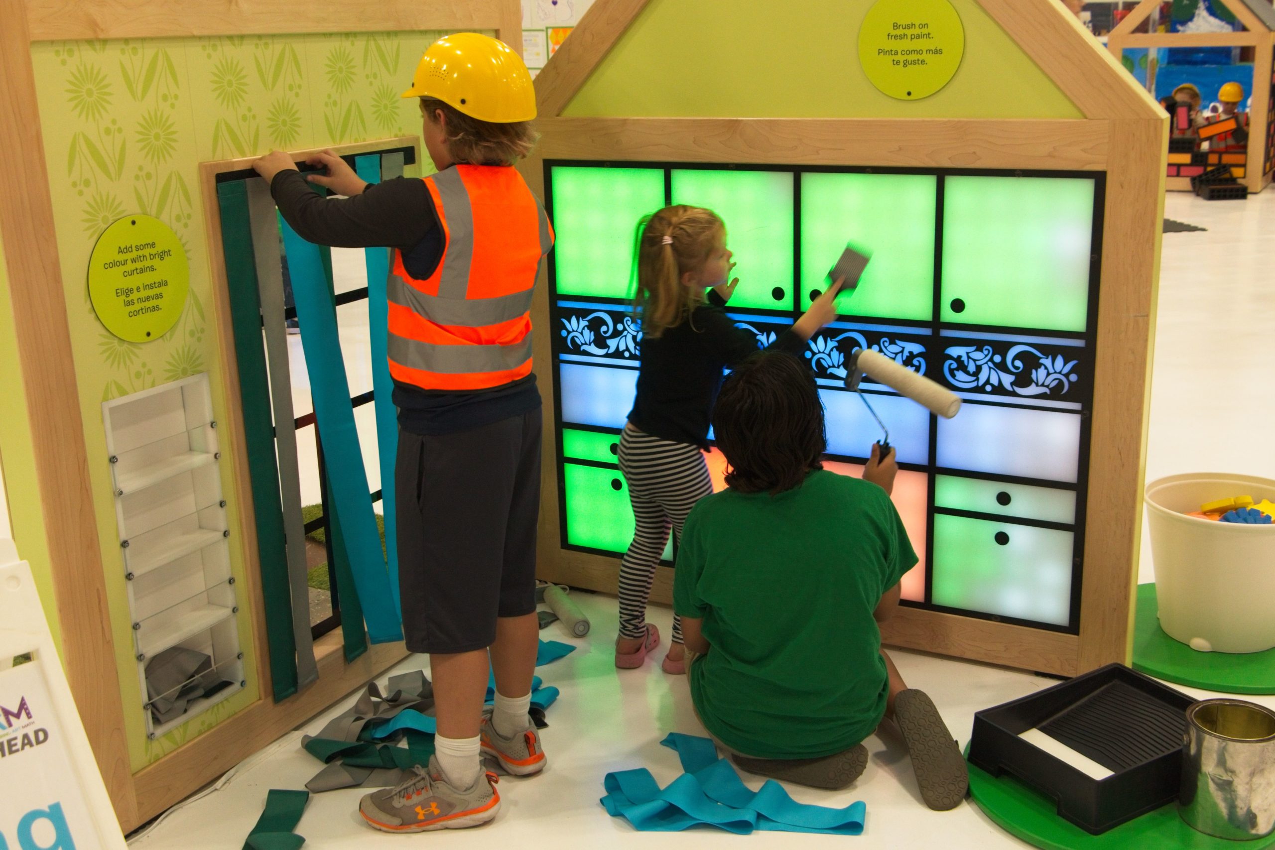 A boy in a hard hat hangs curtains and two children paint a digital color wall