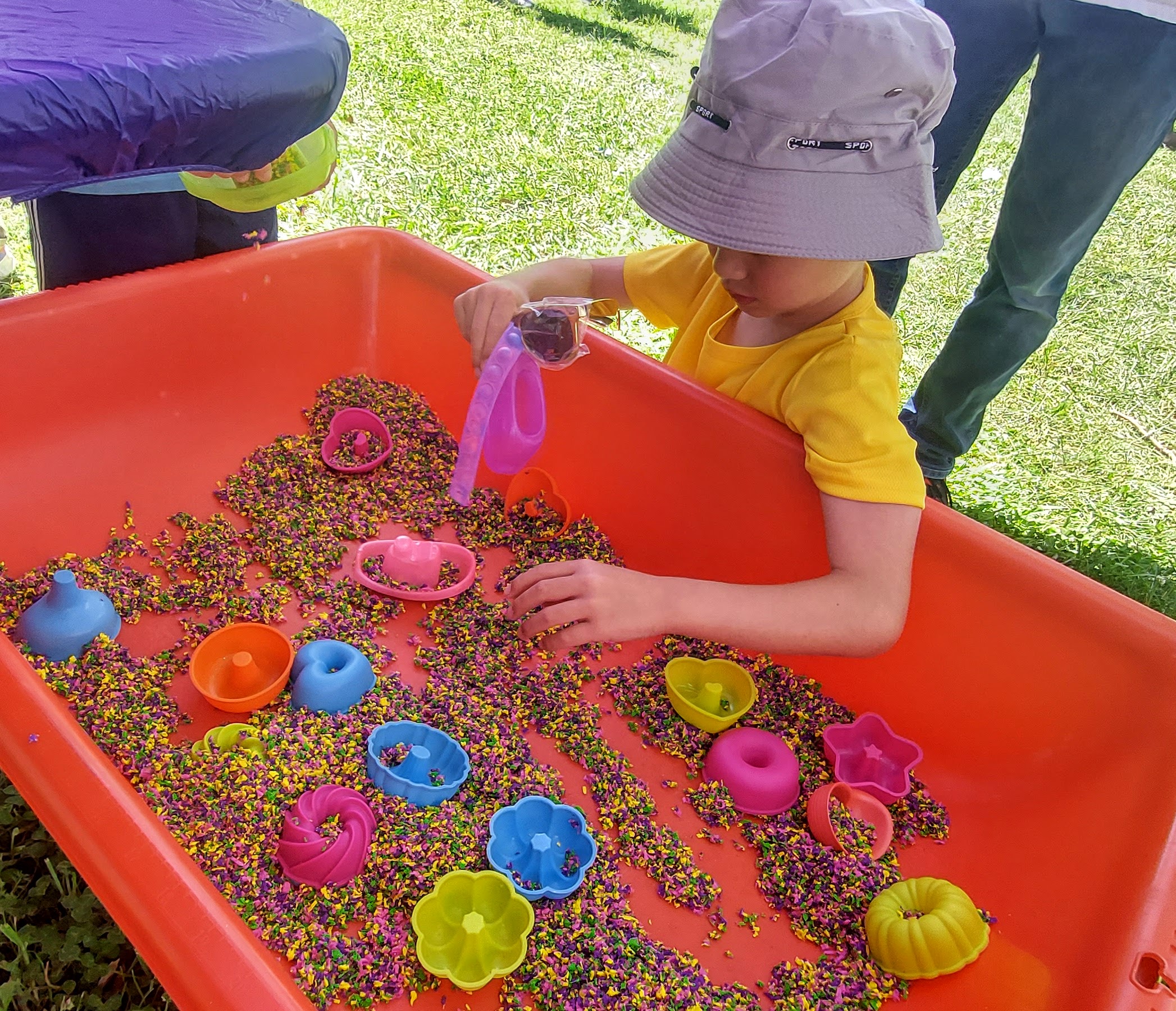 A little boy plays in a sensory bin filled with rainbow fluff and molding toys