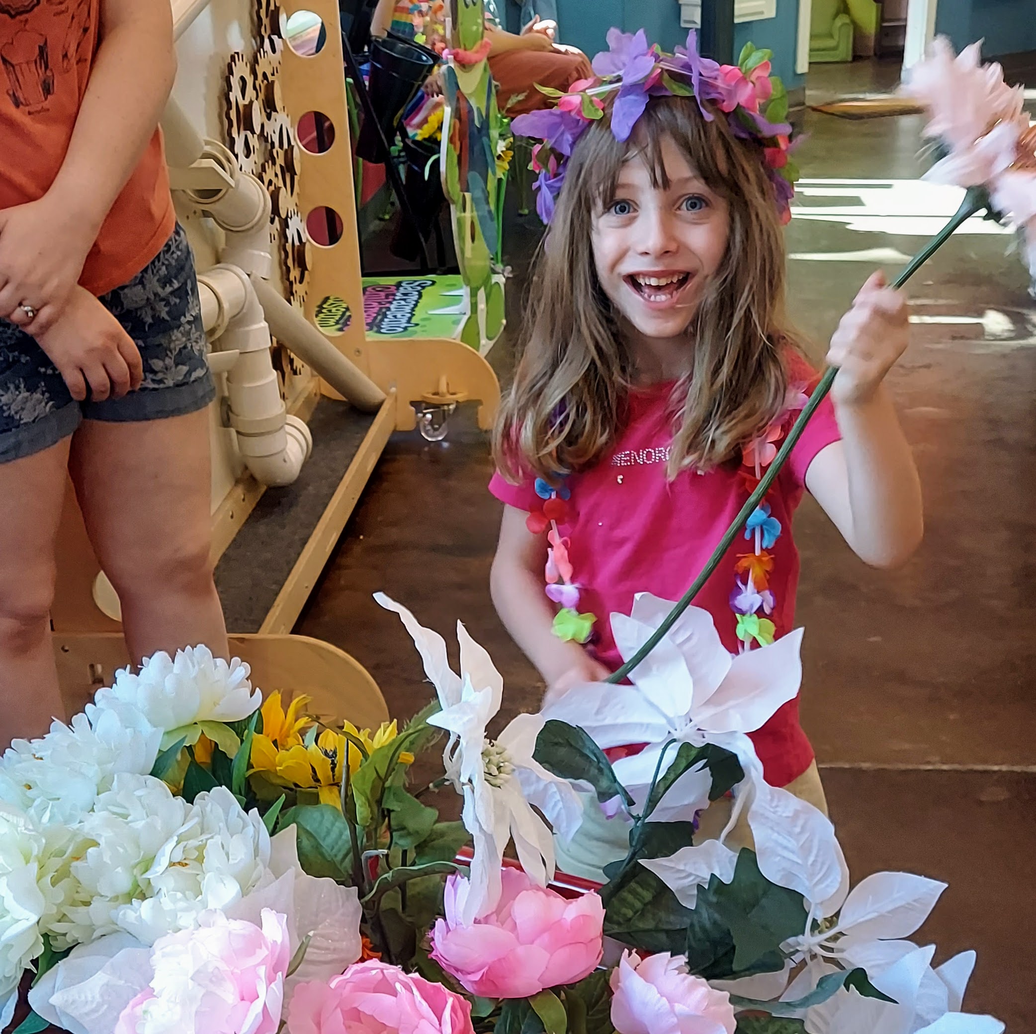 A girl smiles while holding a flower, surrounded by flowers