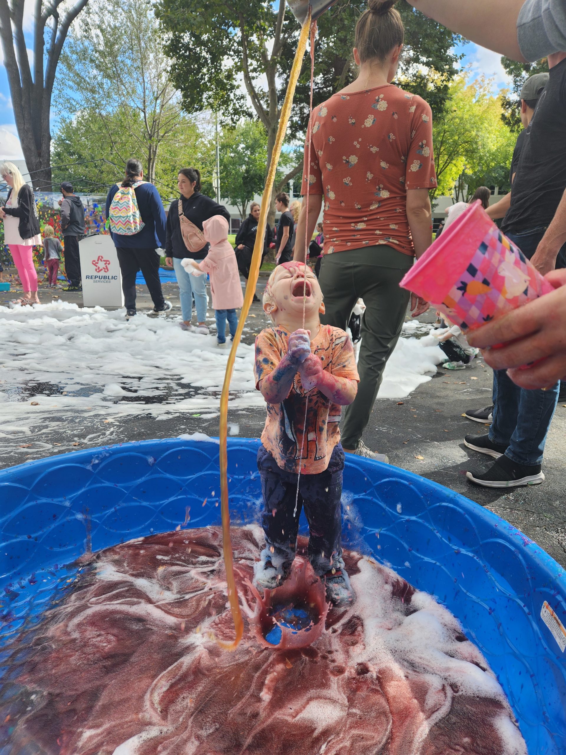 A boy happily dumps slime on himself in a blue baby pool at our Mess Fest event