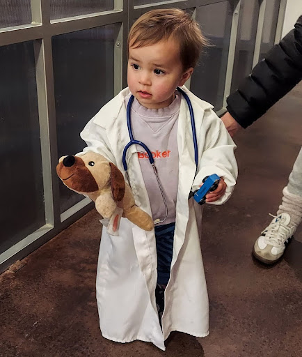 A child dressed in a doctor coat holds a stuffed dog