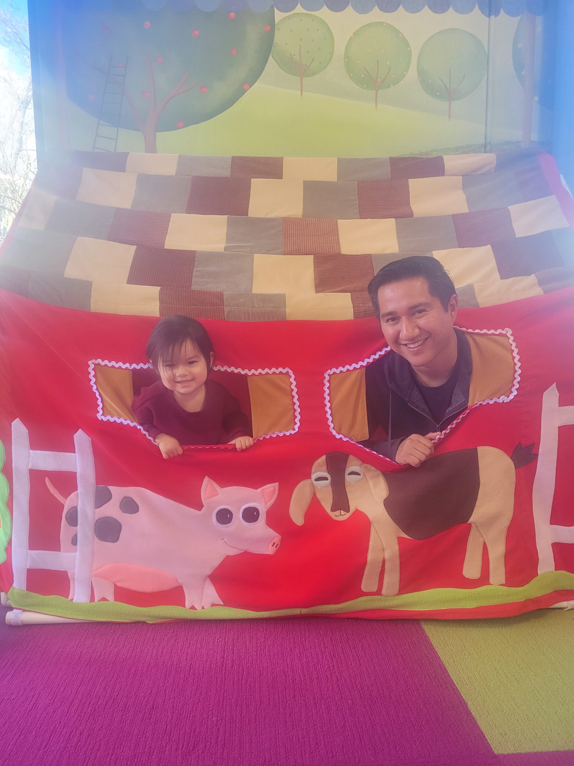 A man and his daughter smile from a fake red barn playhouse
