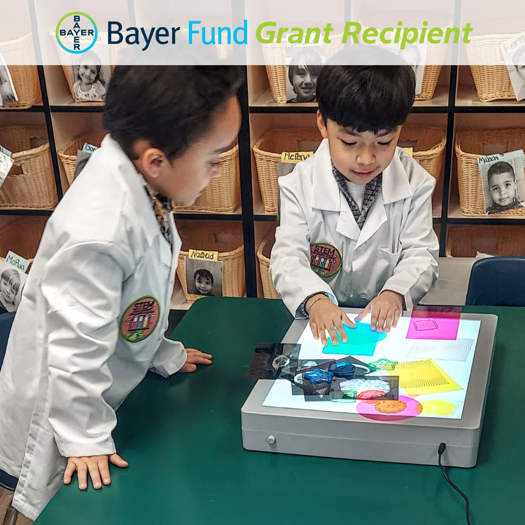 the Bayer logo next to 'bayer fund grant recipient', all over two boys in lab coats doing a STEM activity